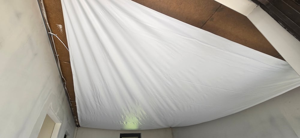 Montage einer Spanndecke: Die weiße Folie wird unter der alten Decke in das Wandprofil eingespannt